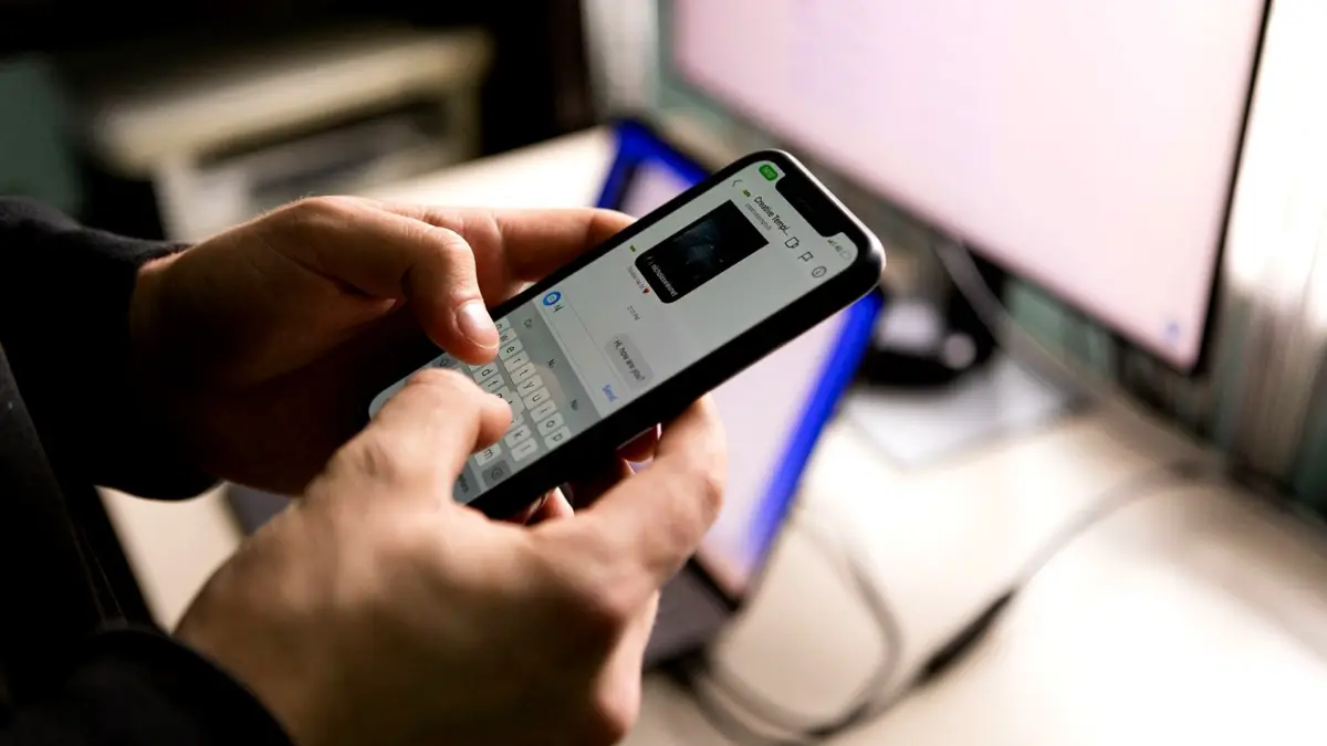 Osoba trzymająca smartfon i pisząca w aplikacji na ekranie