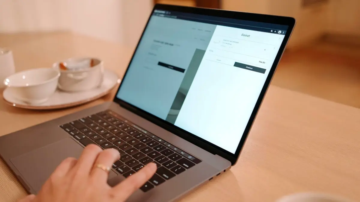 Zbliżenie dłoni osoby pracującej na laptopie postawionym na drewnianym stole