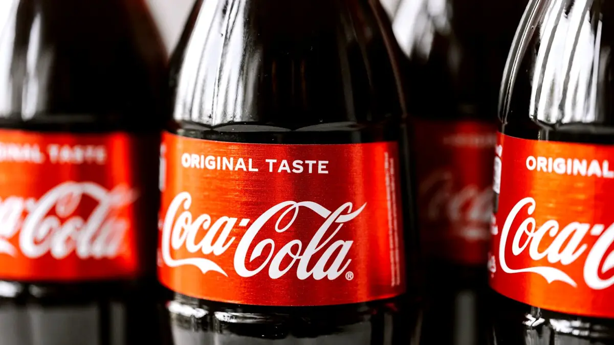 Zbliżenie szklanych butelek Coca-Coli z czerwoną etykietą, ustawionych obok siebie.