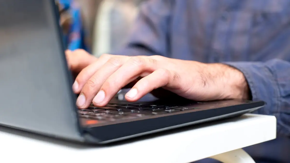Zbliżenie na dłonie wpisujące zapytanie na klawiaturze laptopa