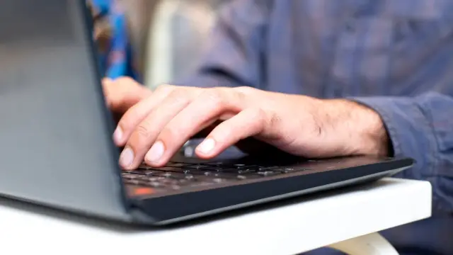Zbliżenie na dłonie wpisujące zapytanie na klawiaturze laptopa