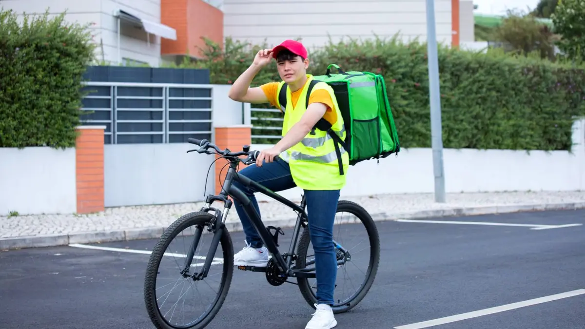 Kurier na rowerze z dużą torbą dostawczą jedzie ulicą w mieście.