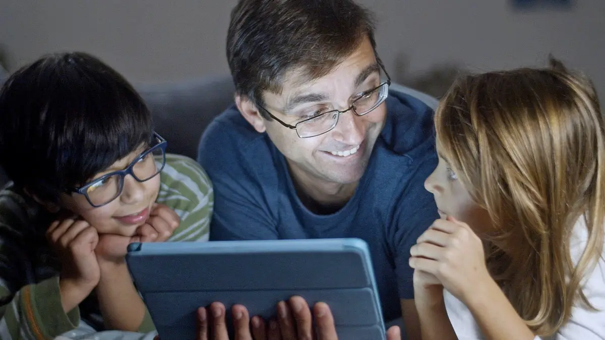Ojciec i dwoje dzieci siedzą razem i patrzą na ekran tabletu