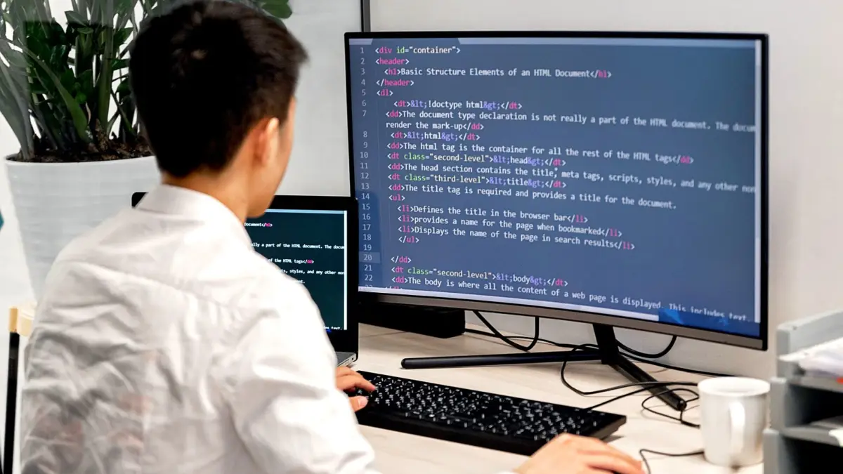 Programista przy dwóch monitorach z kodem pracuje przy biurku