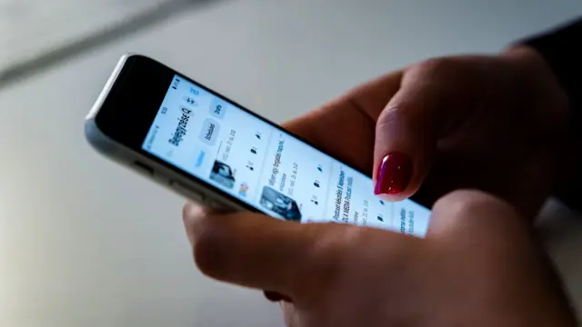 Dłonie trzymające smartfon z przewijaną listą wpisów
