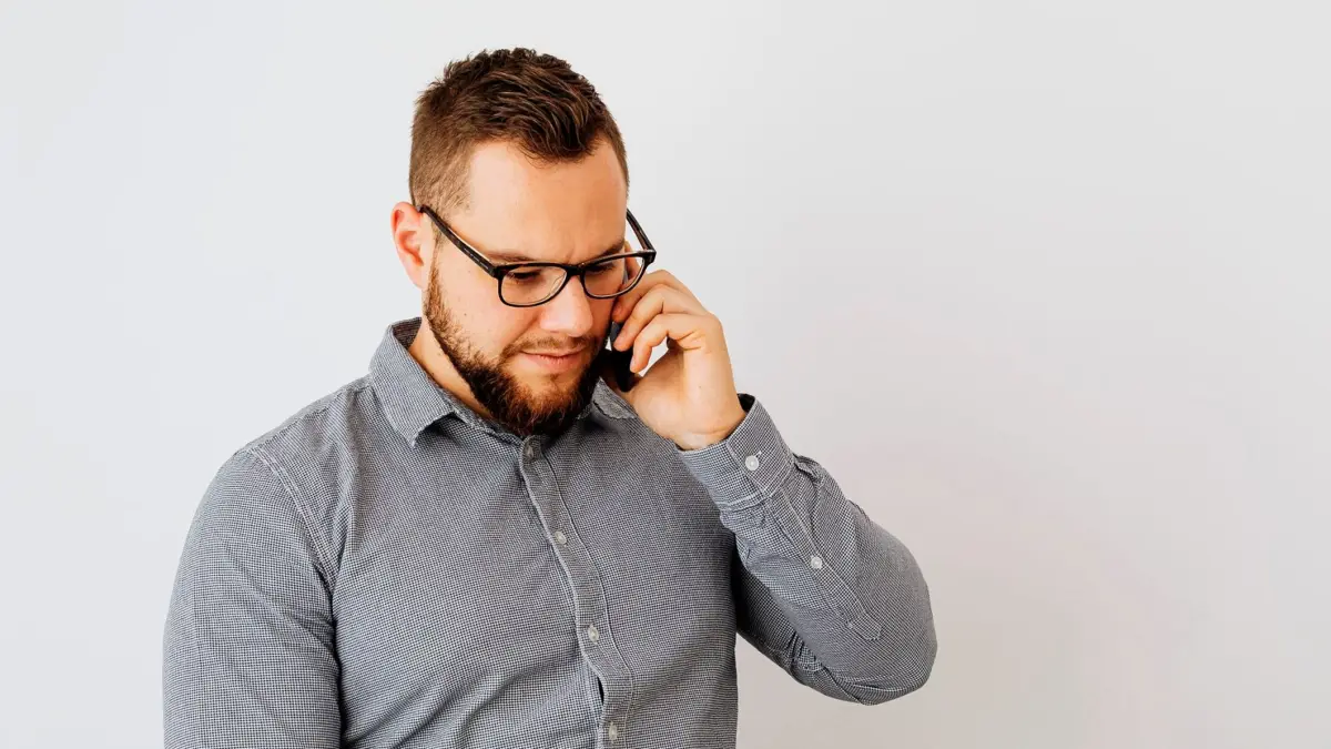 Mężczyzna w okularach rozmawia przez telefon na tle jasnej ściany