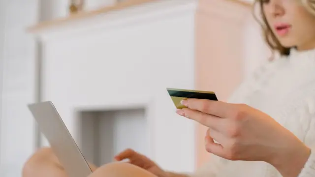 Kobieta przy laptopie sprawdza kartę płatniczą trzymaną w dłoni