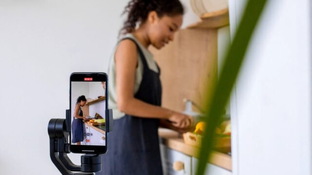 Kobieta nagrywa telefonem na stabilizatorze poradnik kulinarny w nowoczesnej kuchni.