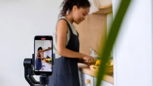 Kobieta nagrywa telefonem na stabilizatorze poradnik kulinarny w nowoczesnej kuchni.