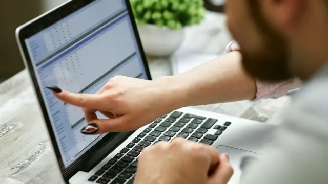 Dwie osoby przy laptopie analizują wykresy z danymi w jasnym biurze.