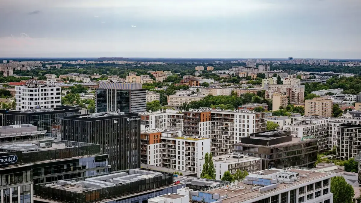Widok z lotu ptaka na Warszawę z nowoczesną i mieszkaniową zabudową wśród zieleni.