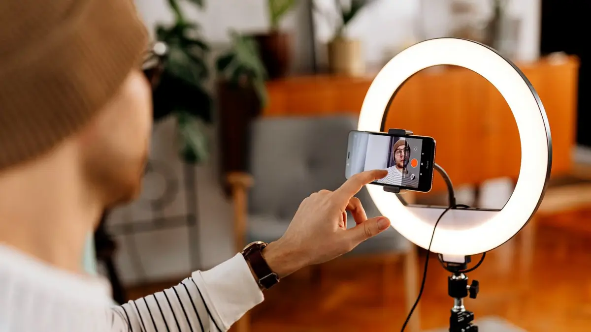 Mężczyzna nagrywa materiał wideo smartfonem ustawionym na statywie w domu.