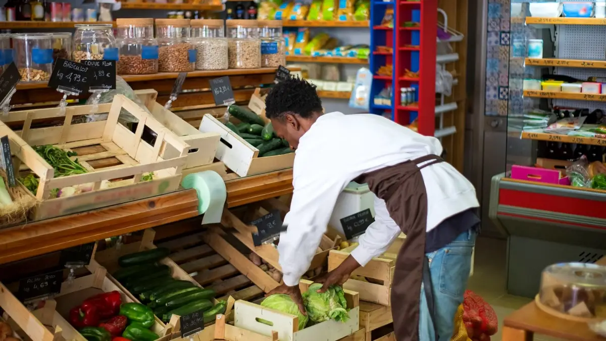 Pracownik sklepu spożywczego układa świeże produkty na półce w alejce.