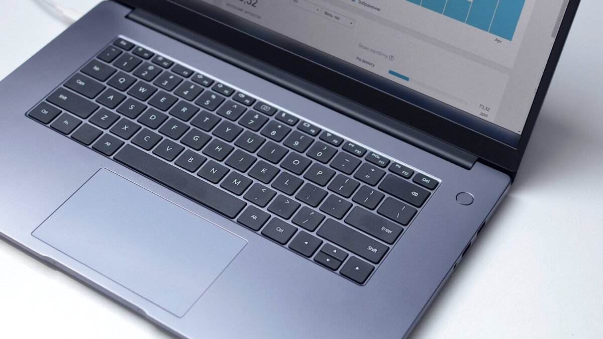 Laptop na białym blacie, na ekranie otwarty program analityczny, ujęcie z góry.