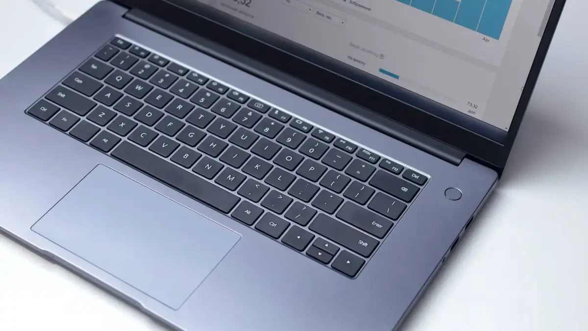 Laptop na białym blacie, na ekranie otwarty program analityczny, ujęcie z góry.