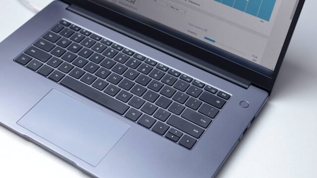 Laptop na białym blacie, na ekranie otwarty program analityczny, ujęcie z góry.