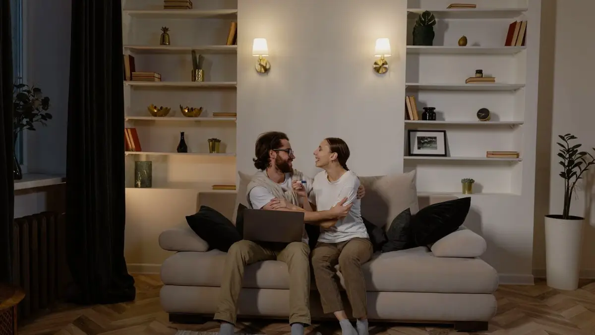 Dwie osoby na kanapie w jasnym salonie oglądają program na ekranie telewizora.