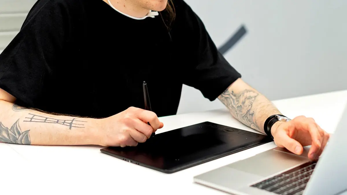Grafik pracuje na tablecie z rysikiem, obok laptop z otwartym projektem