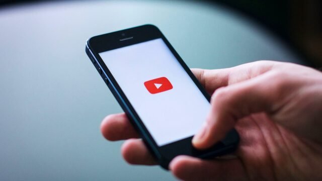 Zbliżenie dłoni z telefonem, na ekranie aplikacja YouTube.