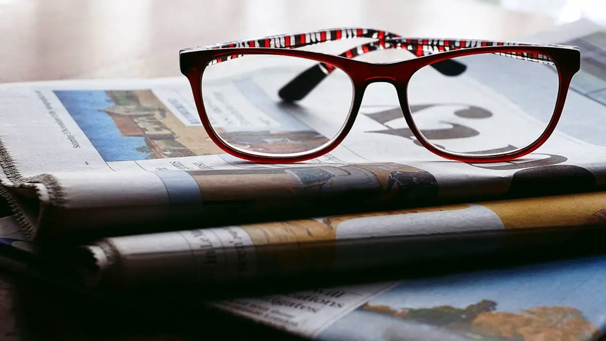Okulary leżące na złożonych gazetach na stole