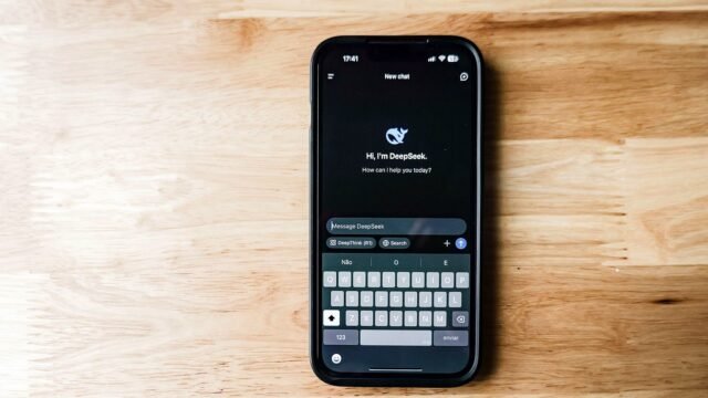 Telefon na drewnianym stole z interfejsem chatbota DeepSeek na ekranie.