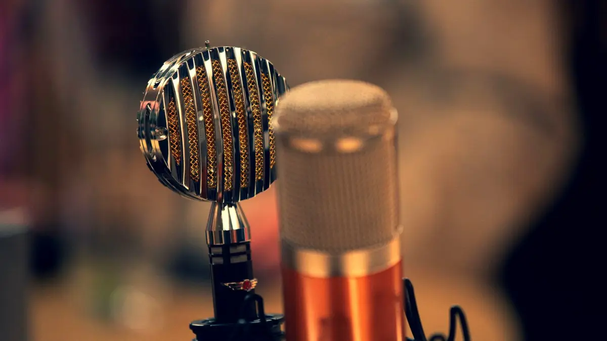 Mikrofon w studiu radiowym, w tle konsola i słuchawki prezentera podczas porannego programu.