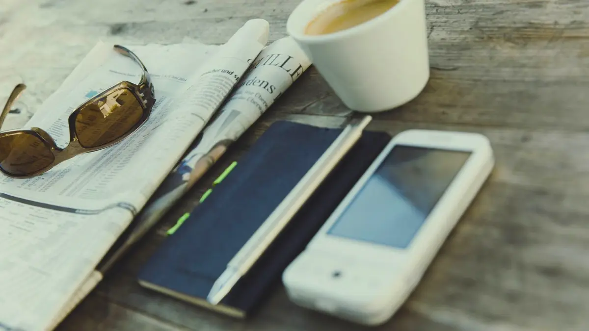 Gazeta, kawa i smartfon na stole przy porannym czytaniu wiadomości