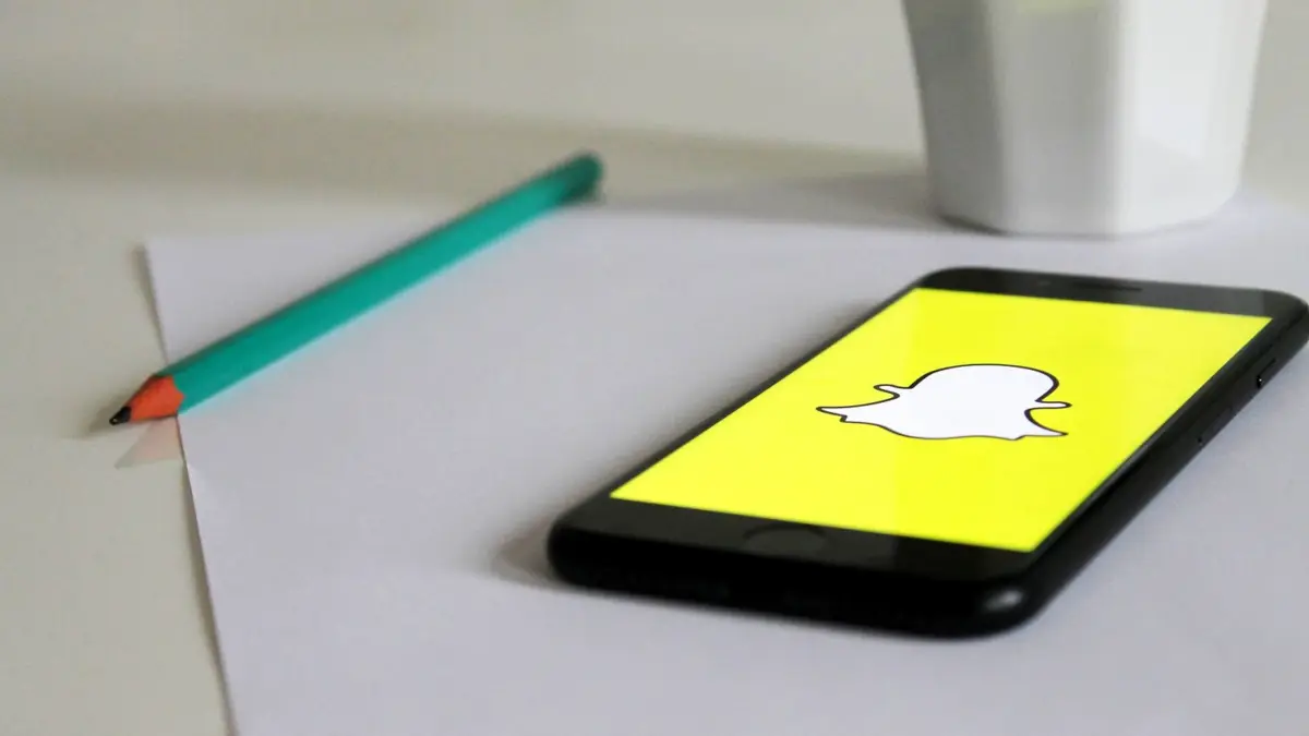 Smartfon z logo Snapchata leżący na biurku obok kubka i ołówka.