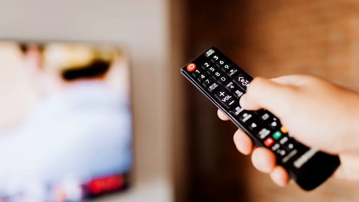 Zbliżenie dłoni trzymającej pilot do telewizora