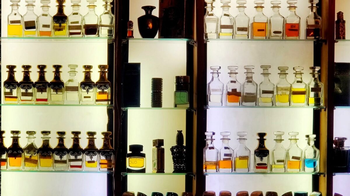 Kolekcja różnych butelek perfum ułożonych na oświetlonej półce.