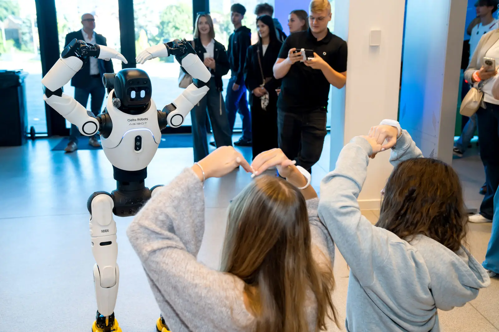 Humanoidalny robot w foyer Hali Urania i uczennice układające dłonie w kształt serca