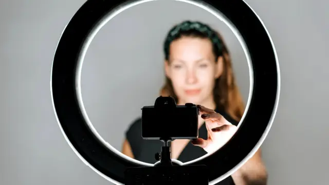 Kobieta ustawia aparat w uchwycie okrągłej lampy przygotowanej do nagrywania filmu.