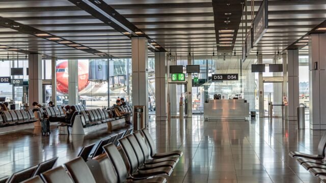 Jasna hala terminalu lotniska z rzędami foteli i samolotem widocznym za oknem