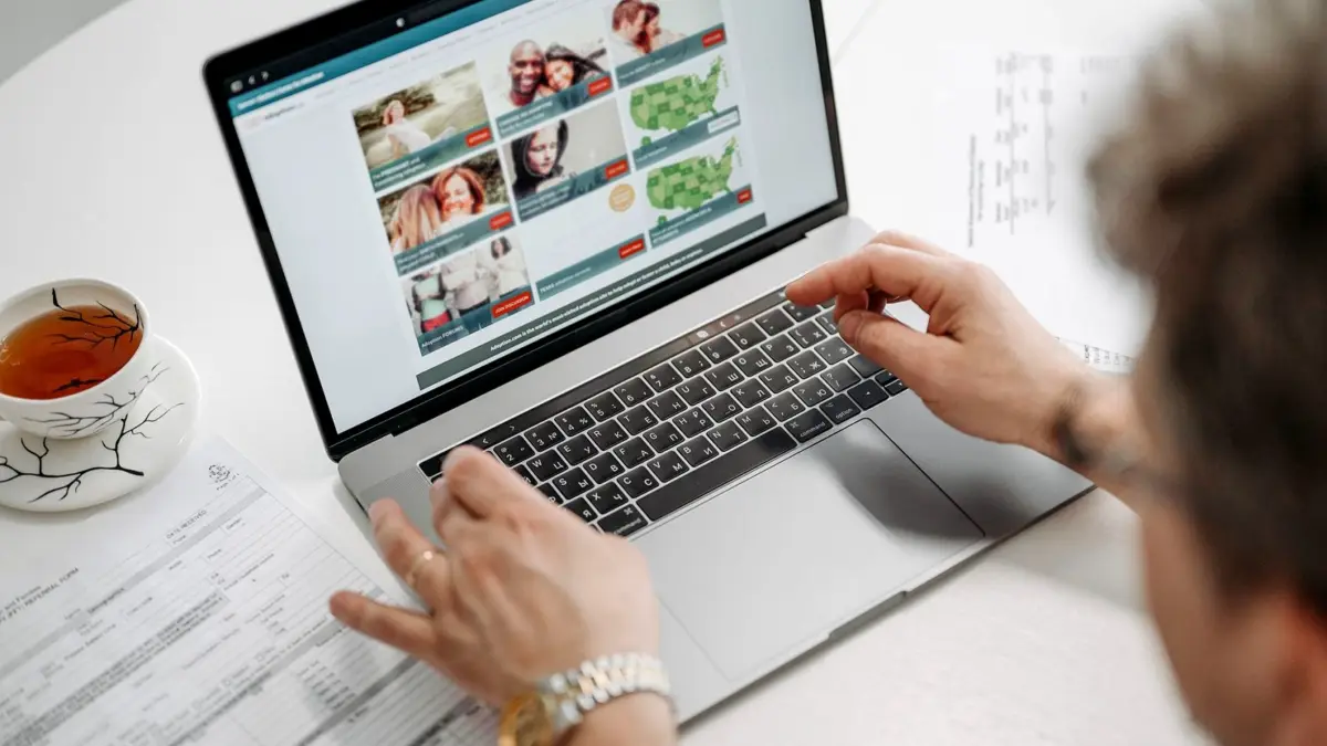 Osoba przegląda stronę internetową na laptopie przy kubku kawy