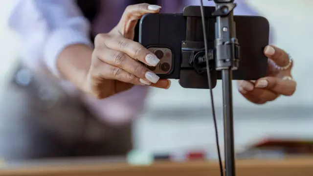 Smartfon na statywie nagrywa pionowe wideo, obok leży sprzęt do montażu.