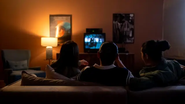 Rodzina siedzi razem na kanapie i ogląda film na dużym telewizorze w salonie.
