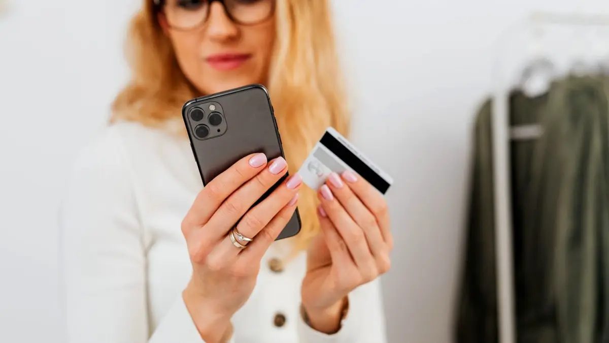 Kobieta trzyma smartfon i kartę płatniczą podczas zakupów w internecie
