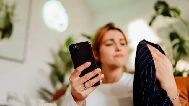 Kobieta siedzi w domu i przewija sklep z ubraniami na ekranie smartfona