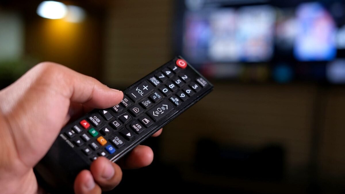 Dłoń trzymająca pilota do telewizora na tle rozmytego ekranu