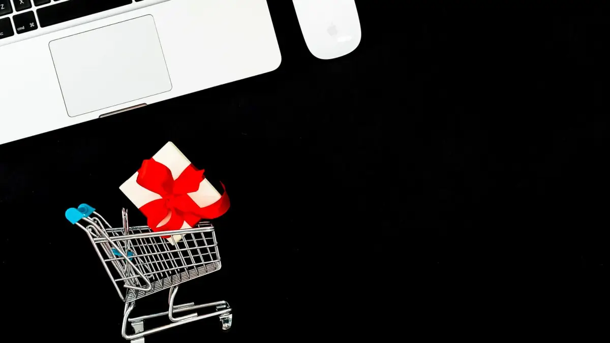 Laptop, mały wózek sklepowy i pudełko z prezentem na czarnym tle