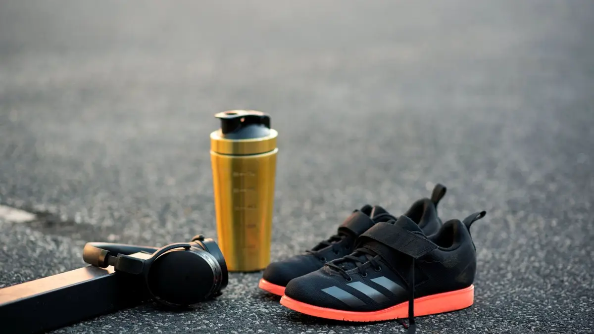 Czarne sportowe buty, słuchawki i shaker na chodniku