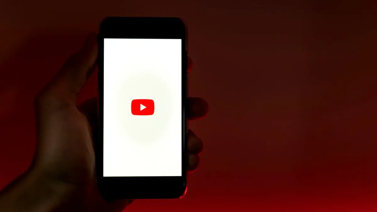 Dłoń trzyma smartfon z aplikacją YouTube na czerwonym tle