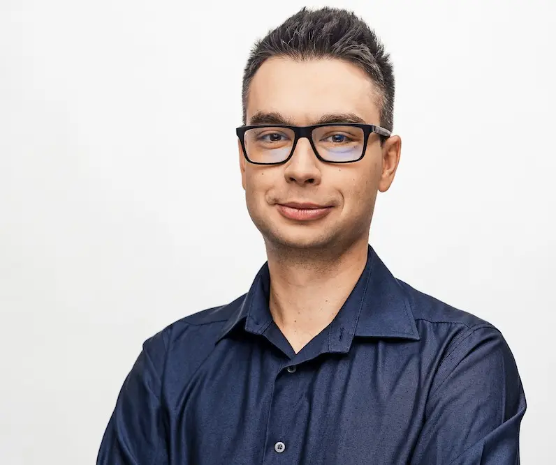 Damian Juszczyk w granatowej koszuli i okularach, portret na białym tle