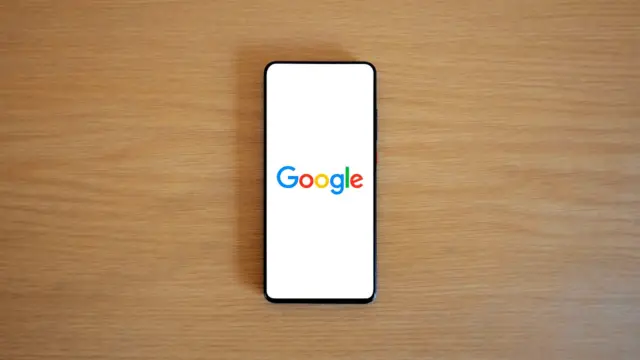 Smartfon ze stroną główną Google leżący na drewnianym blacie