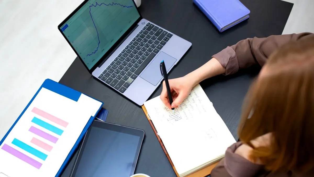 Notatki w zeszycie obok laptopa z wykresami na biurku