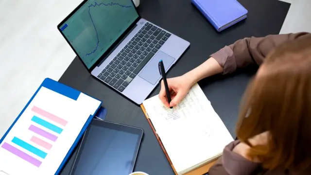 Notatki w zeszycie obok laptopa z wykresami na biurku
