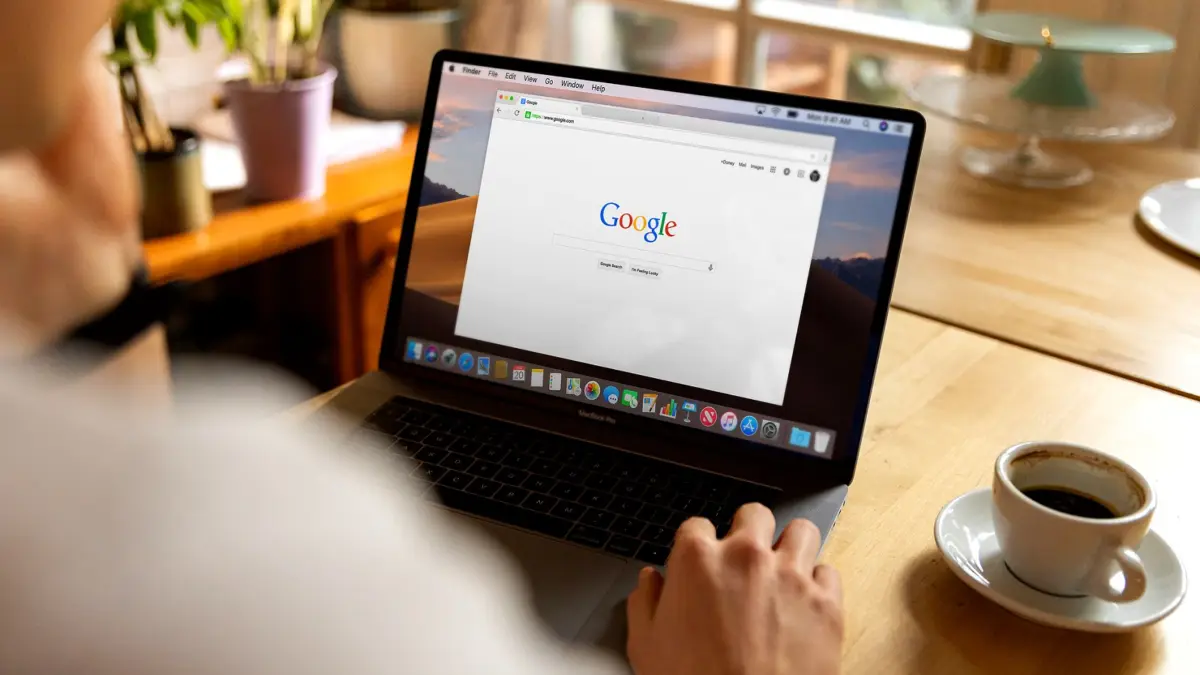 Osoba przy laptopie z otwartą stroną Google, obok kubek, jasne wnętrze
