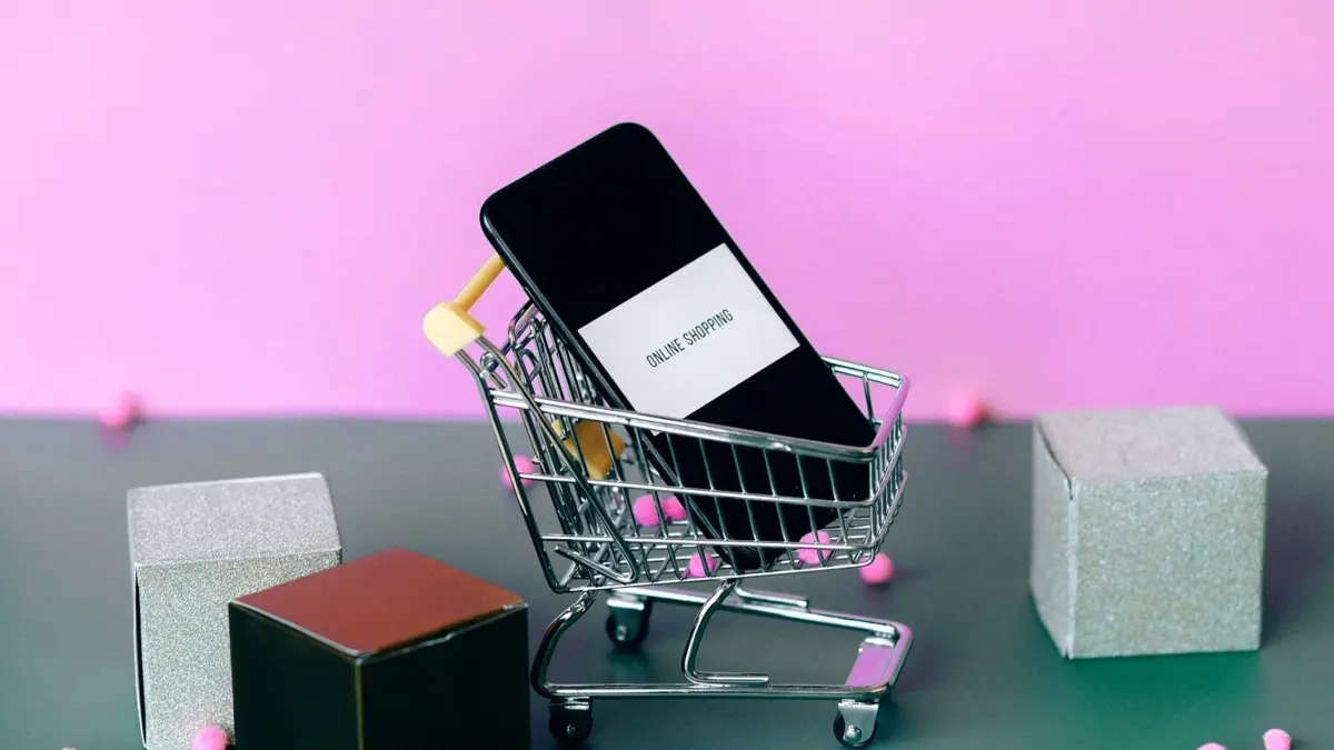 Smartfon z ikoną wózka sklepowego i małym wózkiem zakupowym obok