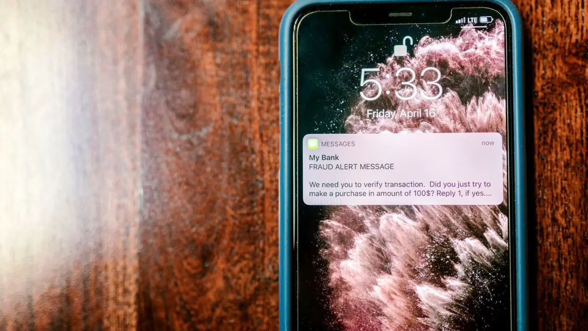 Smartfon na drewnianym blacie z powiadomieniem ostrzegającym przed oszustwem