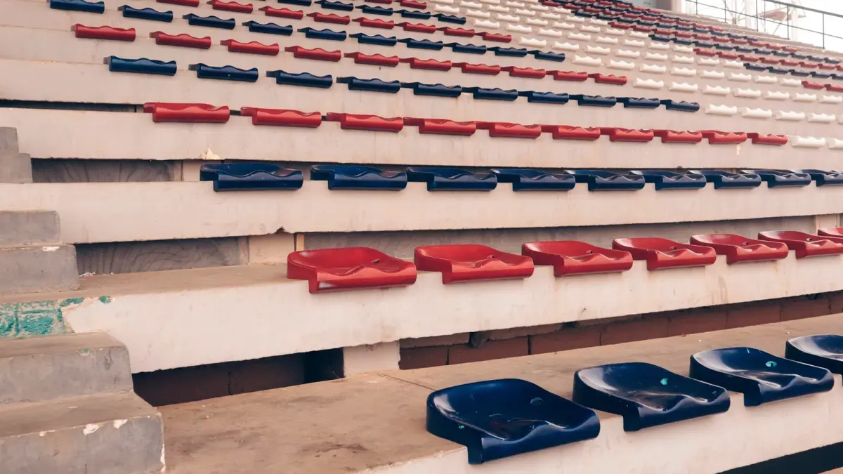 Rzędy pustych czerwonych, niebieskich i białych krzesełek na stadionie